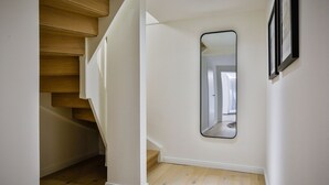 A hallway with a wooden staircase, a white wall, and a mirror. - Lornsendüne - Modern apartment in an absolutely beachfront location in Westerland with (Sylt)
