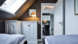 Een slaapkamer met twee bedden, een dakraam, een schilderij en uitzicht op een keuken.