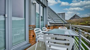 Een balkon met een tafel en stoelen, grote ramen en uitzicht op de lucht en verre gebouwen.