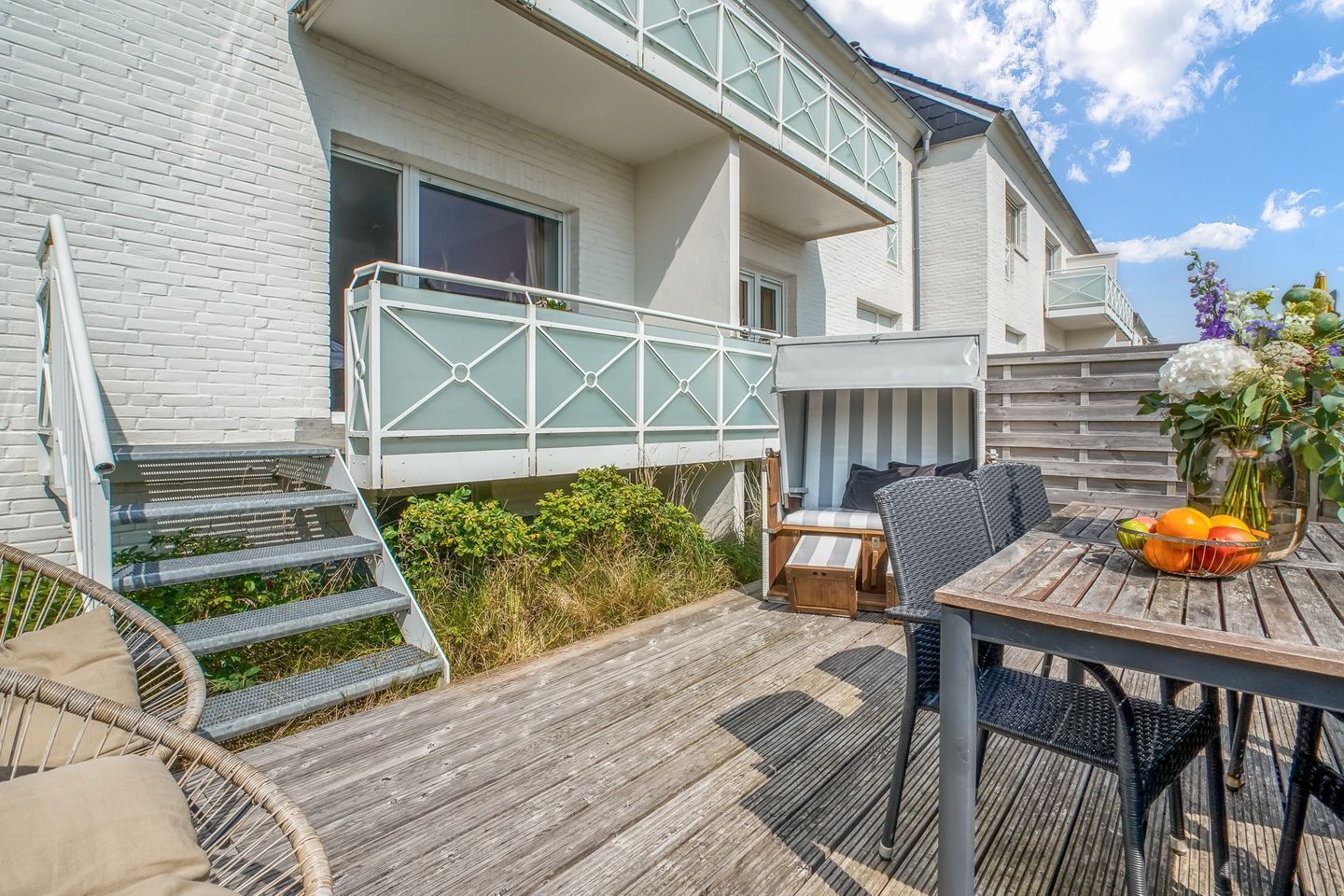 Ein modernes Haus mit einer Holzdielen-Terrasse, einer überdachten Sitzgelegenheit und einem Tisch mit Obst.