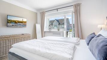 Een slaapkamer met een bed, een rieten stoel, een raam met gordijnen en een schilderij aan de muur.
