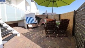 Eine Terrasse mit Tisch, Stühlen, einem gestreiften Liegestuhl und einem grünen Sonnenschirm.