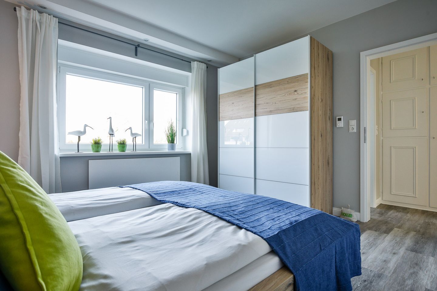 A bedroom with a bed, a window with curtains, a view of the street, and a door.