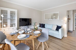 A modern living room with a dining table set for six, a light blue sofa, and a television.