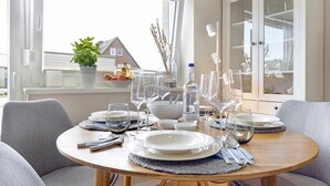 A dining table set with plates, glasses, and cutlery, a bottle of MAGNUS water, and a fruit bowl. - Njørd - Haus Möwe, Deutschland (Hörnum (Sylt))