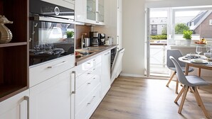 A modern kitchen with white cabinets, a Bosch dishwasher, and a dining area with grey chairs and a wooden table. - Njørd - Haus Möwe, Deutschland (Hörnum (Sylt))