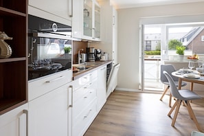 A modern kitchen with white cabinets, a Bosch dishwasher, and a dining area with grey chairs and a wooden table.