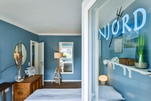 A bedroom with a bed, a dresser, a mirror, a lamp, and a window with the word "NORD" on it.