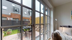 A room with large windows, a stone wall, and a view of a garden and building outside. - Ellis beach house Sylt (Hörnum (Sylt))
