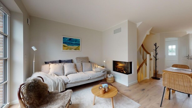A modern living room with a sofa, a fireplace, a dining area, and a staircase. - Ellis beach house Sylt (Hörnum (Sylt))