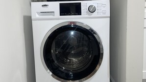 Una lavadora de carga frontal blanca Summit SPWD2202W en un cuarto de lavado con piso de madera y una planta en la parte superior.