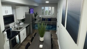 Cocina compacta con electrodomésticos modernos, comedor con mesa y sillas, y vista a una piscina por una ventana.