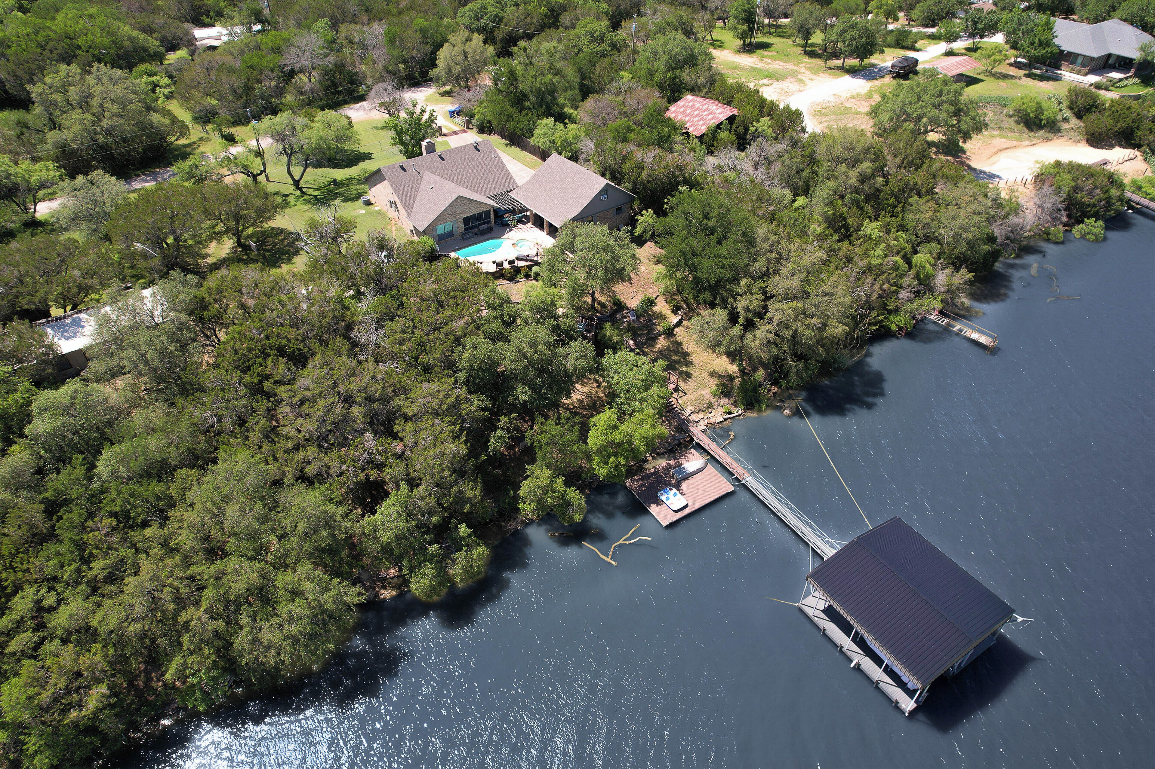 Vista aérea de una casa con un muelle que se adentra en un lago, rodeada de árboles frondosos.