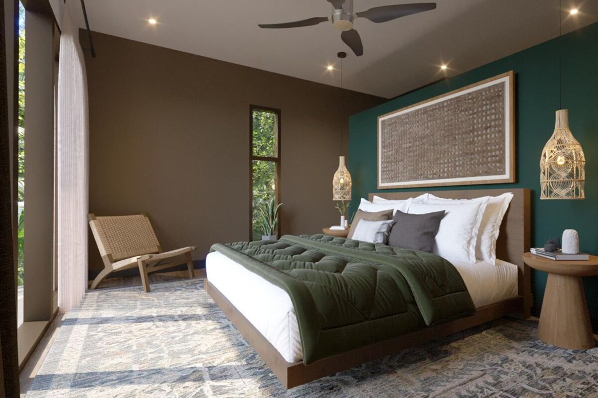 A bedroom with a bed, a chair, a bedside table, a wall-mounted light, and a ceiling fan.
