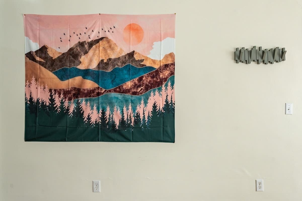 A tapestry with a mountainous landscape and birds, displayed on a wall.