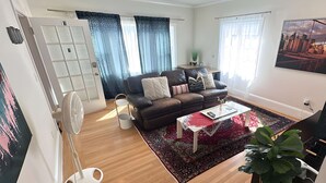Un salón con sofá, mesa de centro y un ventanal con cortinas.