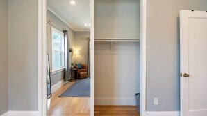 Un pasillo con piso de madera que conduce a una habitación con cama, mesita de noche y lámpara.