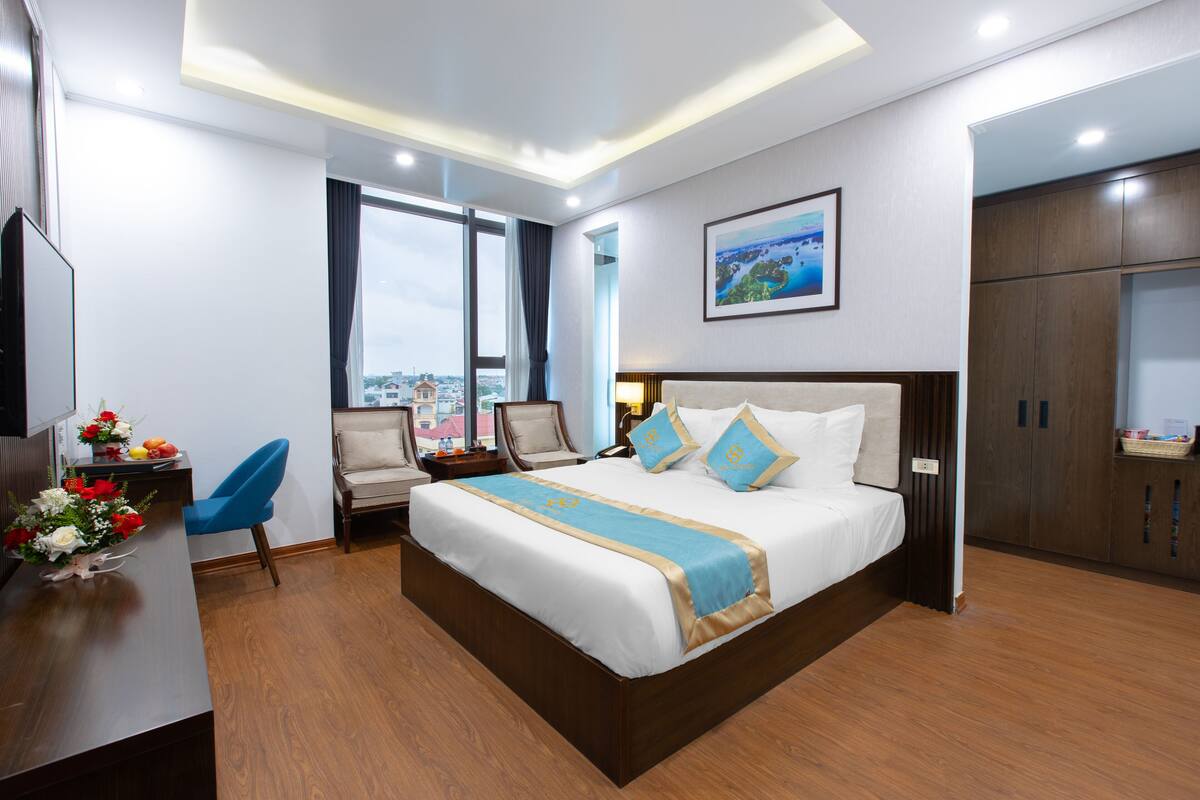 Een hotelkamer met een groot bed, een bureau met stoel, een televisie en een raam met uitzicht op de stad.