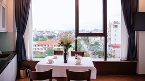 Un comedor con una mesa dispuesta para dos personas, un jarrón con flores y vistas a la ciudad a través de amplias ventanas.