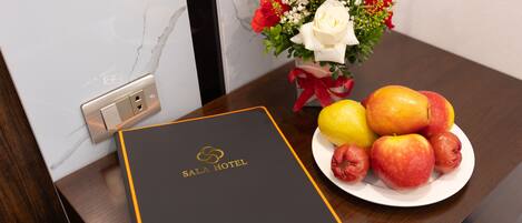 A room with a wooden table, a white plate with fruits, a vase with flowers, and a black and gold folder labeled "SALA HOTEL".