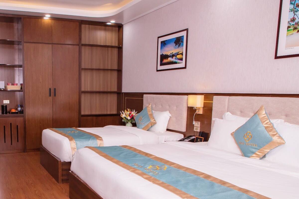 Een hotelkamer met twee bedden, een houten garderobe, een nachtkastje, een lamp en een lijstje aan de muur.