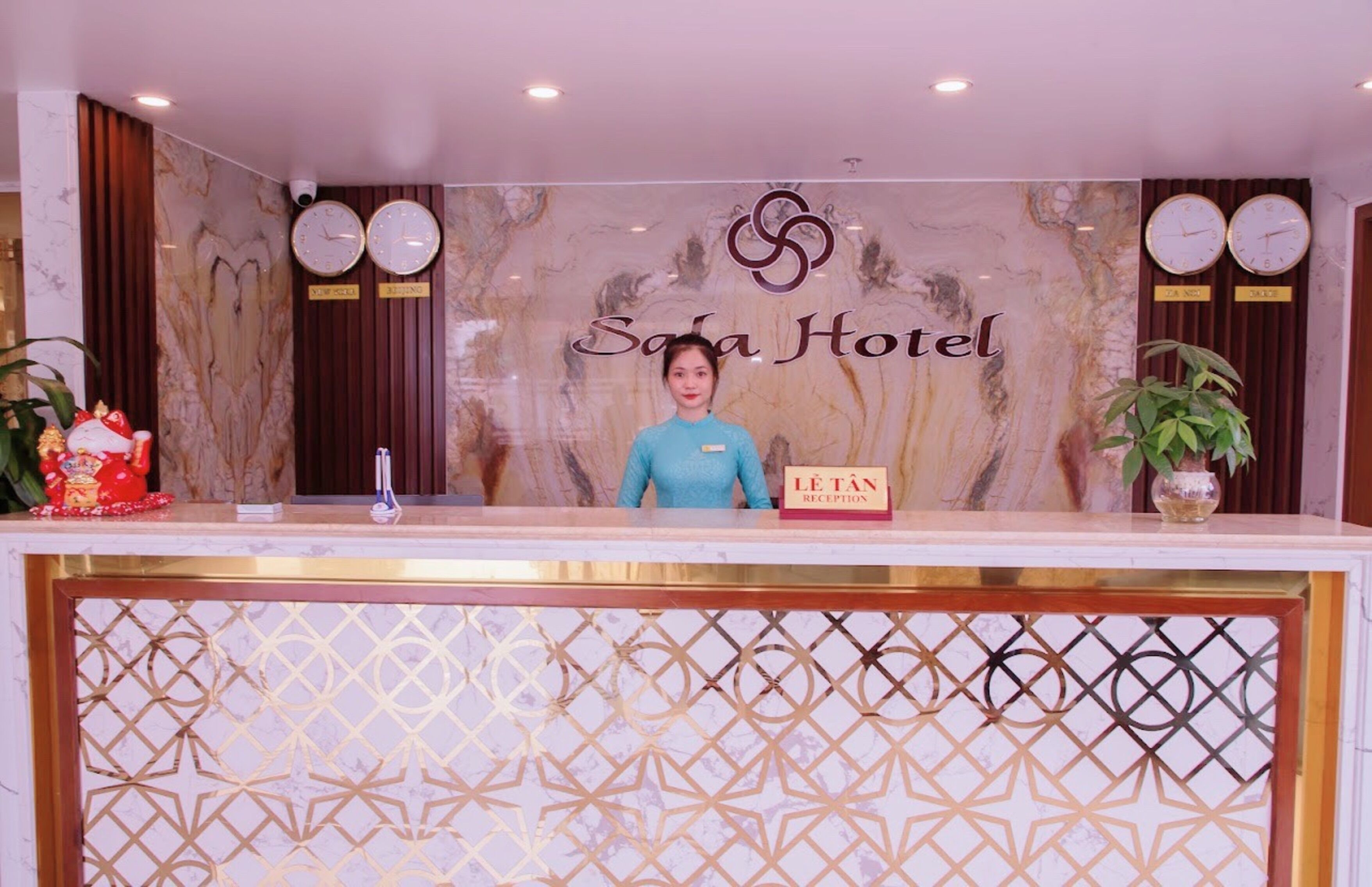 A hotel reception desk with a marble wall, clocks, and a sign reading "Sala Hotel".