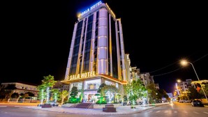 Un hotel moderno con un llamativo letrero que dice "SALA HOTEL", que presenta una fachada vertical con ventanas iluminadas y una entrada bien iluminada.