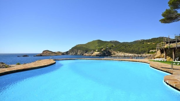 A clear blue swimming pool with a curved edge, surrounded by a stone deck and a wooden fence. - Rental apartment with sea view in Aiguafreda, Begur (Begur)