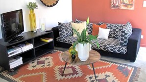 Un salon avec un canapé noir, une table basse, un meuble pour la télévision et un tapis à motifs.