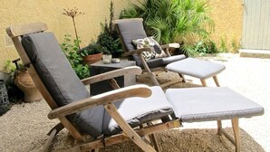 Un espace patio comprenant deux fauteuils en bois et une petite table, le tout entouré de plantes en pot et d’un mur à motifs.