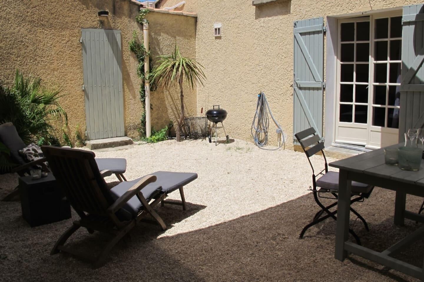 Un espace patio aménagé avec deux chaises longues, une table et un barbecue.