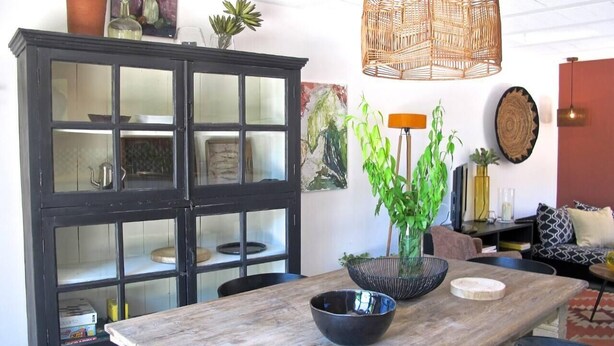 Un coin repas avec une table en bois, un meuble noir et un luminaire suspendu en osier.