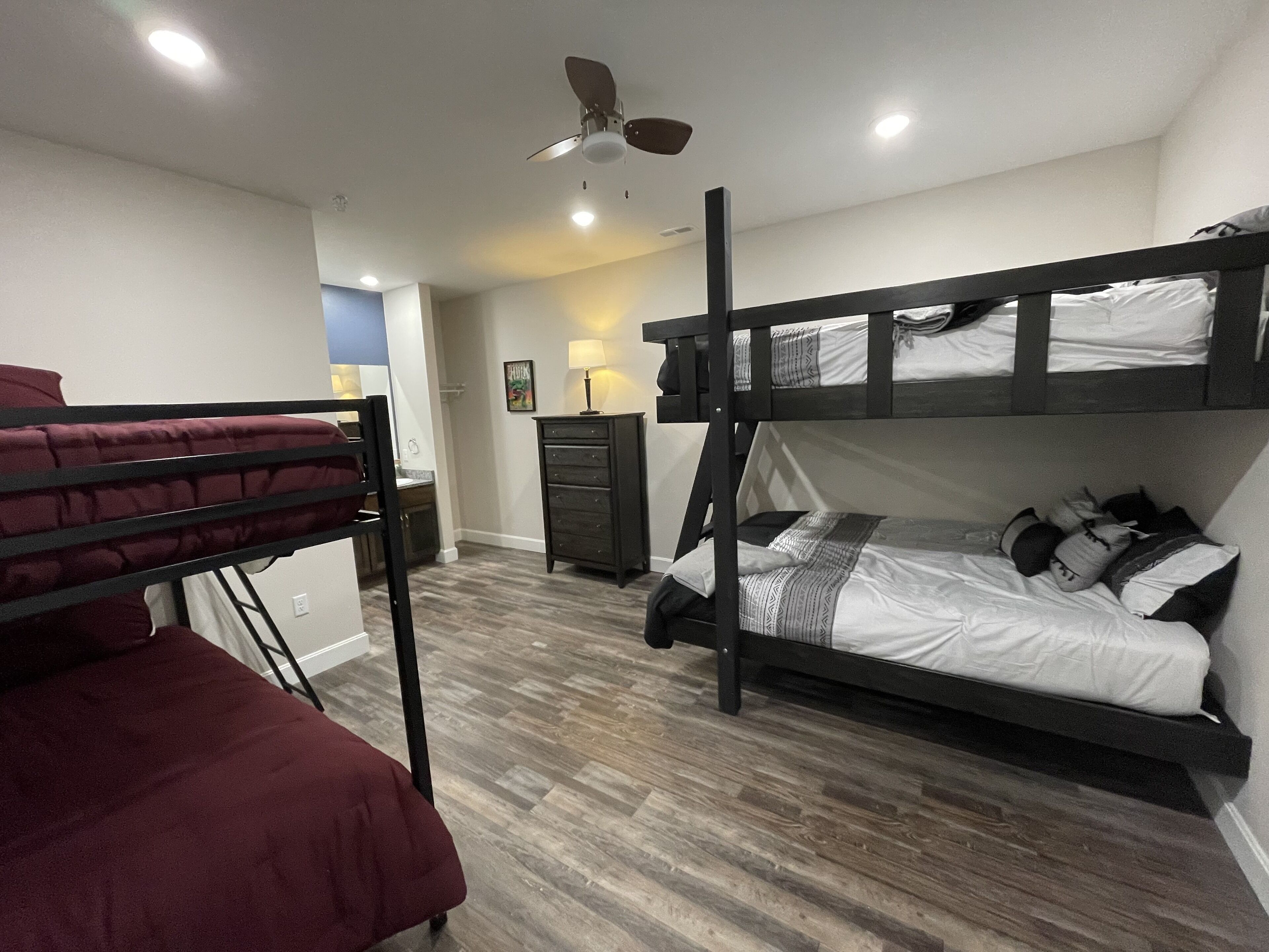 A bunk bed room with a ceiling fan, a desk, and a dresser.