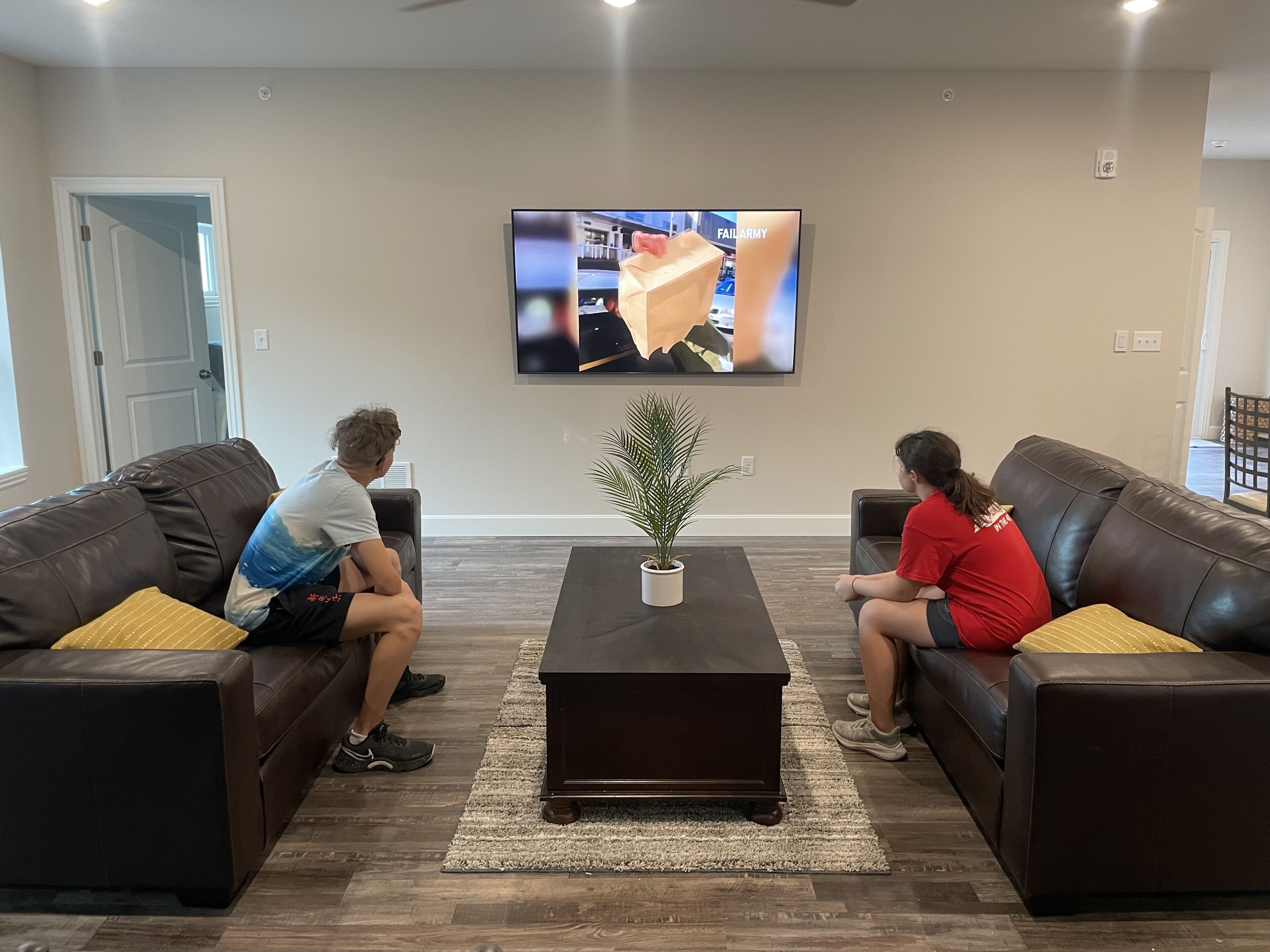 A living room with two brown leather sofas, a coffee table, and a television mounted on the wall.