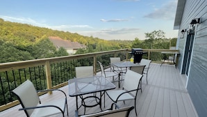 Um terraço com mobiliário para área externa, churrasqueira e vista para uma área arborizada.