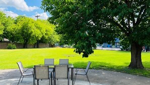 A patio with a table and chairs, surrounded by a grassy yard and trees. - Regency Inn & Suites Houston East I 10 (Houston)