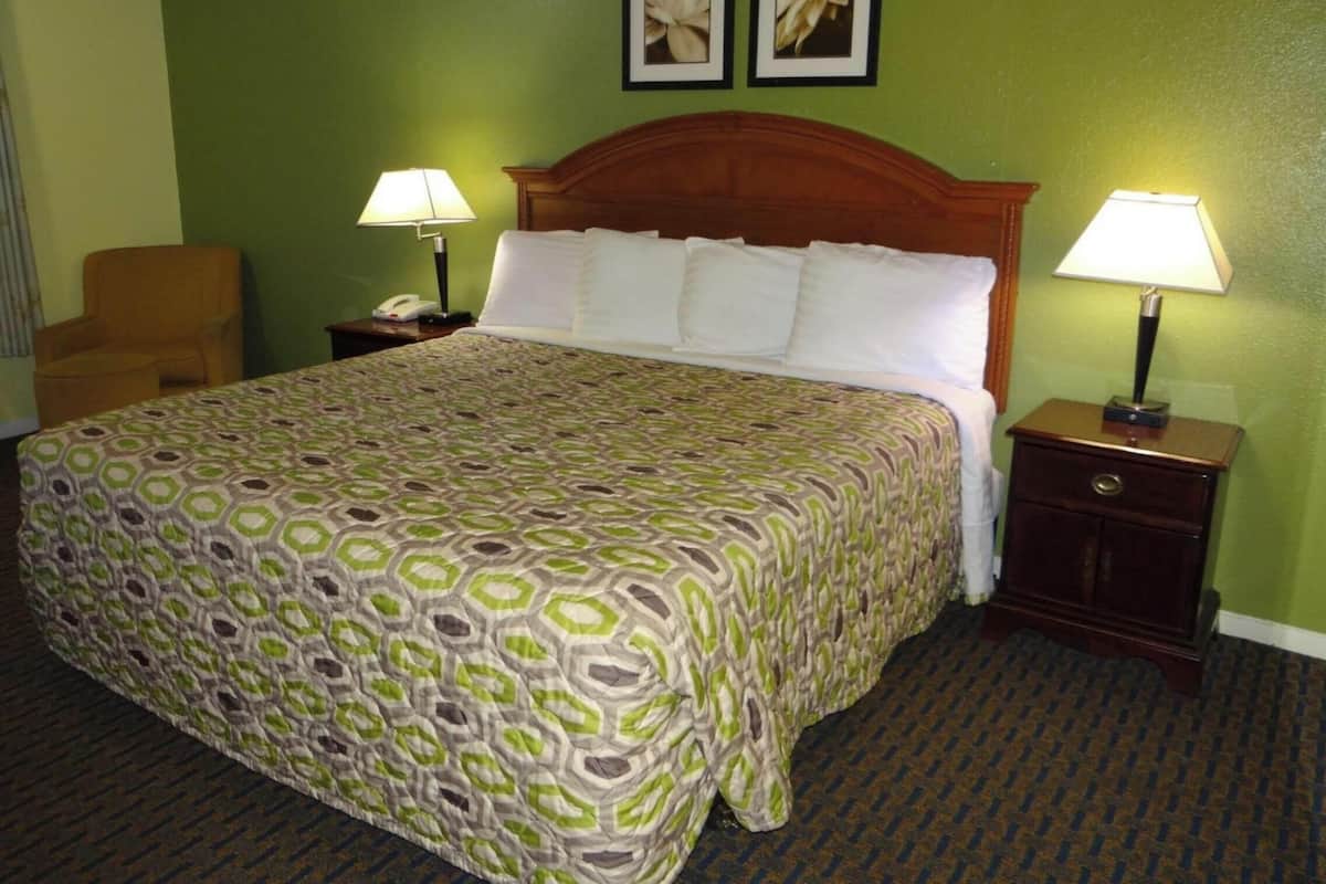 Ein Hotelzimmer mit einem großen Bett, zwei Nachttischen, einem Sessel und grünen Wänden.
