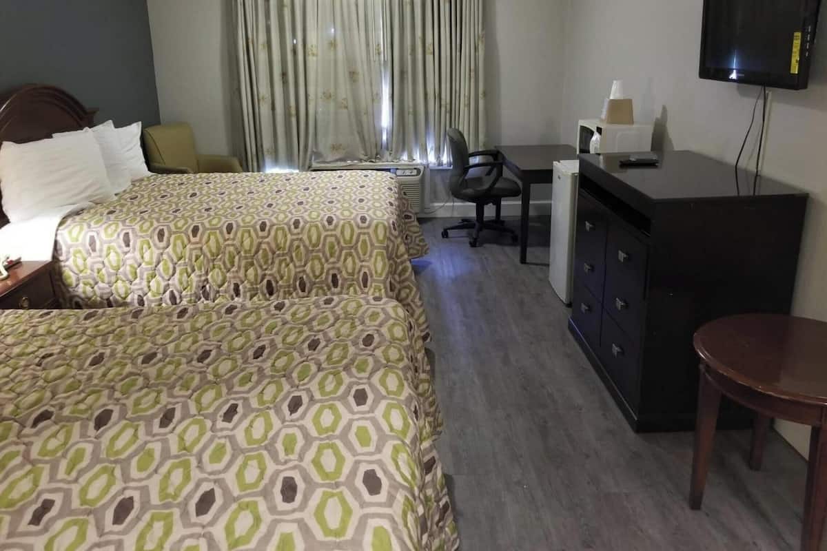 Ein Hotelzimmer mit zwei Betten, einem Schreibtisch, einem Stuhl, einem Fernseher und einem Kleiderschrank.