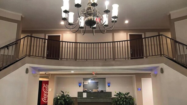 A hotel lobby with a registration desk, a chandelier, a Coca-Cola refrigerator, and a staircase. - Regency Inn & Suites Houston East I 10 (Houston)