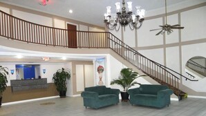 A spacious lobby with a reception desk, two green sofas, a chandelier, a ceiling fan, and a staircase. - Regency Inn & Suites Houston East I 10 (Houston)