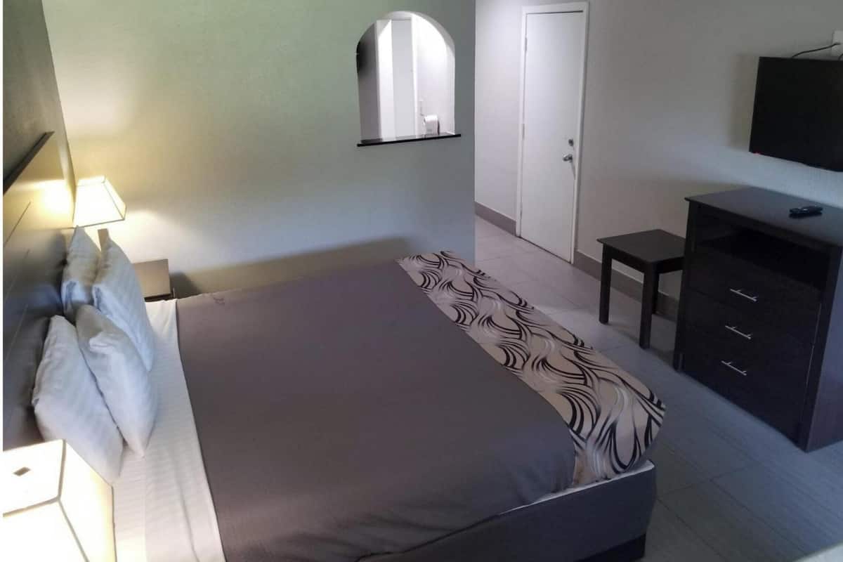 Ein Schlafzimmer mit Bett, Schreibtisch, Stuhl, Fernseher, Spiegel und Kleiderschrank.