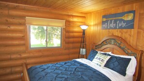 Ein Schlafzimmer in einer Blockhütte mit Bett, Fenster, Lampe und einer Wandtafel.