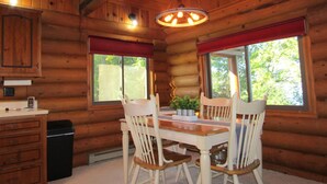 Ein rustikales Holzhäuschen mit Esszimmer, Stühle, einer Kristallleuchtre und Fenstern mit roten Vorhängen.