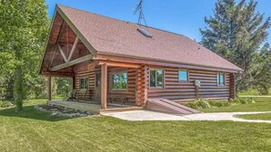 Eine Blockhütte mit geneigtem Dach, einer Veranda mit Rampe und einer kleinen Holzterrasse.