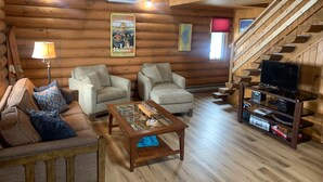 Ein rustikales Blockhaus-Interieur mit zwei Sofas, einem Couchtisch, einem Fernseher und einer Treppe.
