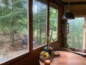 A wooden interior with large windows, a table with a bowl of fruit, and a hanging lamp.