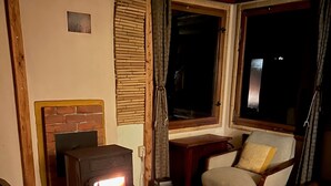 Un salón acogedor con estufa de leña, un sofá cómodo, una mesita y una ventana con cortinas.