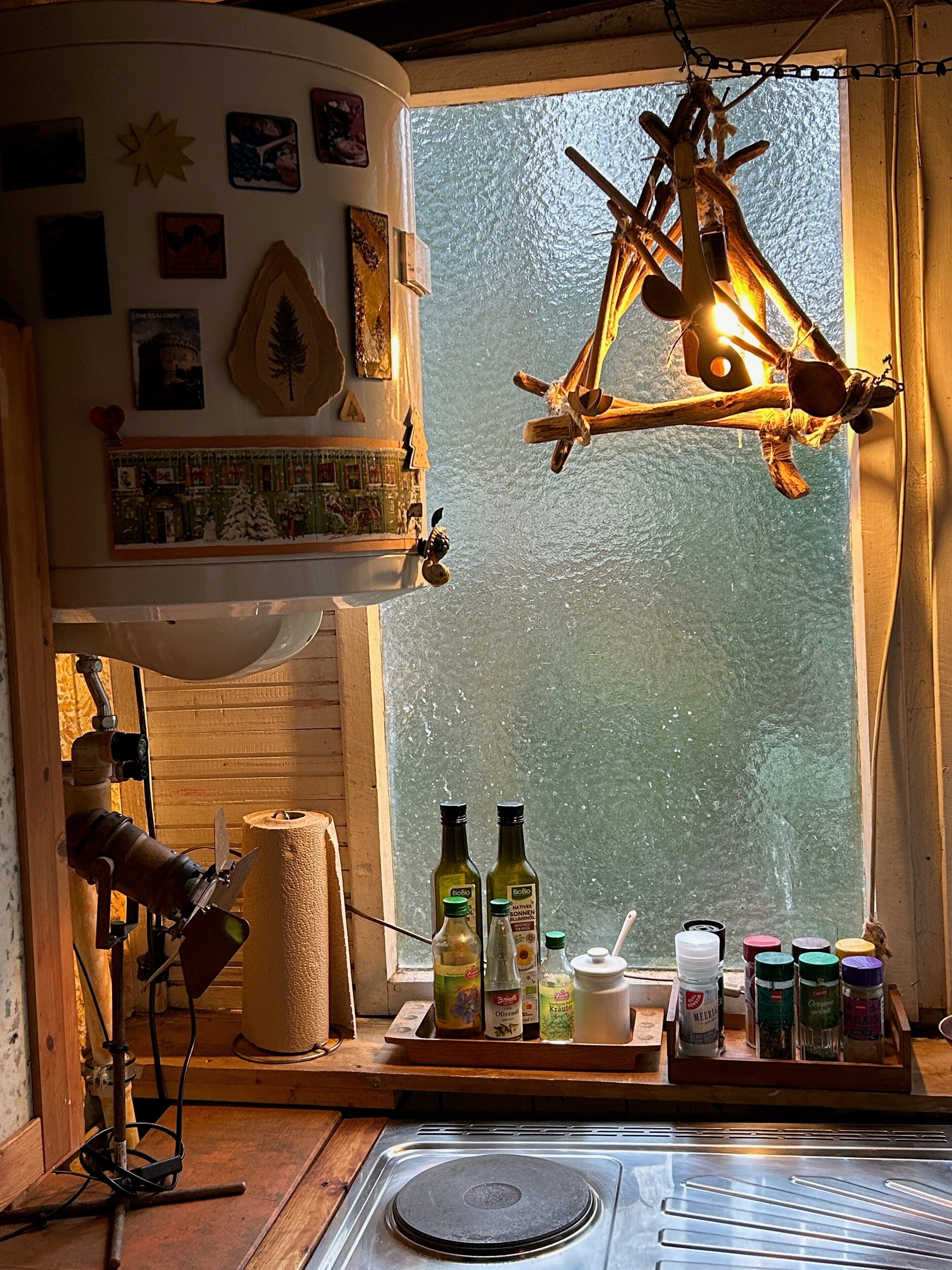 A kitchen with a wooden stove, a hanging light fixture, and various kitchen items on the windowsill.