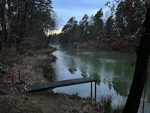 Ein Fluss mit einer Holzanlegestelle, umgeben von Bäumen und blauem Himmel.