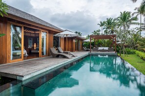 Una villa de madera con piscina, sillones de descanso y una zona de estar cubierta.